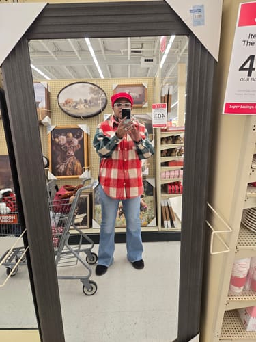 Customer taking a mirror selfie in a store wearing the red and green plaid shacket with jeans.