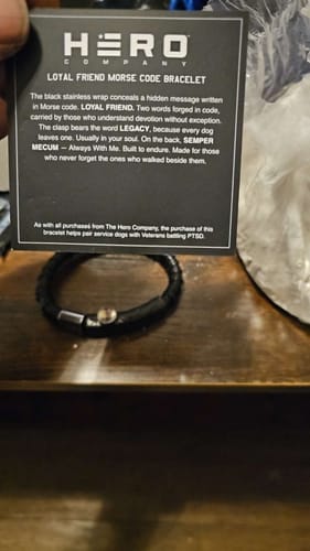 Customer holding the descriptive card next to the black Loyal Friend Morse Code bracelet on a table.
