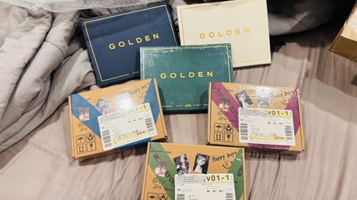 Customer's three BTS V - LAYOVER album packages laid out on a bed with other albums.