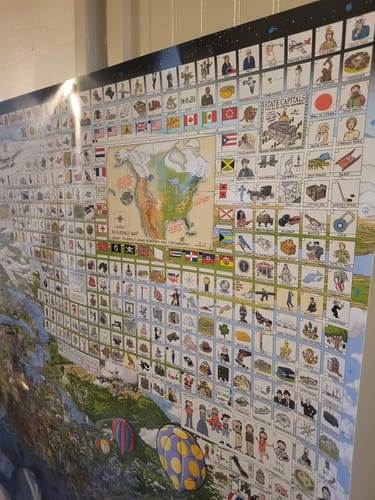 Customer's large World's Greatest Search & Discover poster on a wall, showing its dense grid of colorful illustrations.