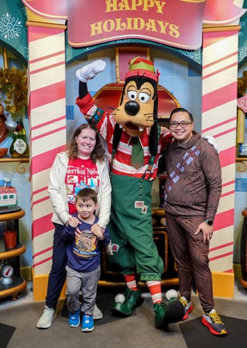Customer wearing 'The Chewie' – Performance Joggers, posing with their family and Goofy at a holiday event.