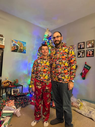 Customer and their son wearing matching Disney and Pixar Cars 'Sponsors of Speed' hoodies in front of a Christmas tree.