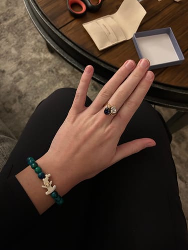 Reviewer's hand wearing the Navae Birthstone Ring, showing a dark blue pear-cut and clear radiant-cut stone on a gold band.