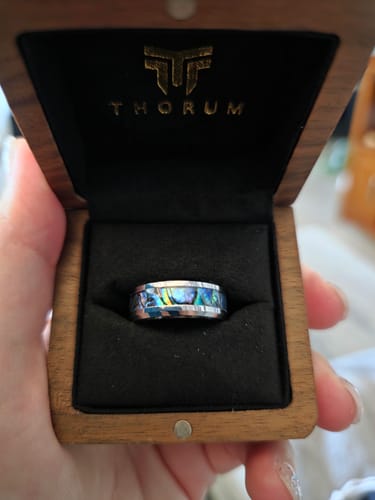 A customer's Angler ring with a vibrant abalone inlay, shown inside its open wooden box.