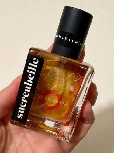 Reviewer holds the square bottle of Serenity perfume, showing its shimmery golden liquid.