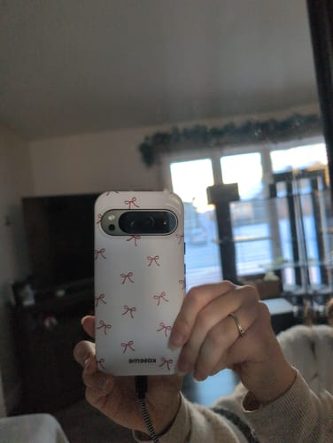Customer taking a mirror photo, showing their phone in the white Roselyn case with a red bow pattern.