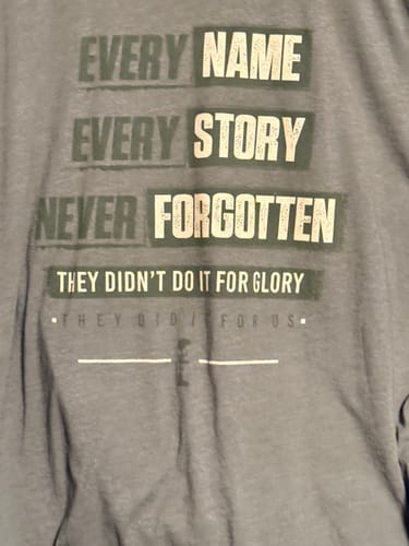 Close-up of a customer's grey T.V.P. Elite Membership shirt showing the text 'Every Name, Every Story, Never Forgotten.'
