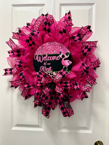 Customer's Flamingo Sign at the center of a large, vibrant pink and black wreath on a white door.
