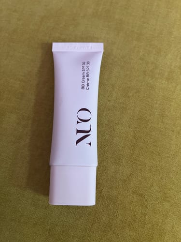 Customer's white tube of BB Cream SPF30 standing on a solid green surface.