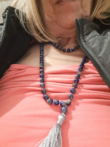 Une cliente porte son Collier Mala Lapis Lazuli, montrant les perles bleues et le pompon gris.