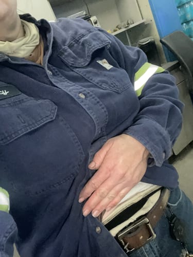 A reviewer at their industrial job wearing the brown leather Double Roller belt with a work shirt and jeans.