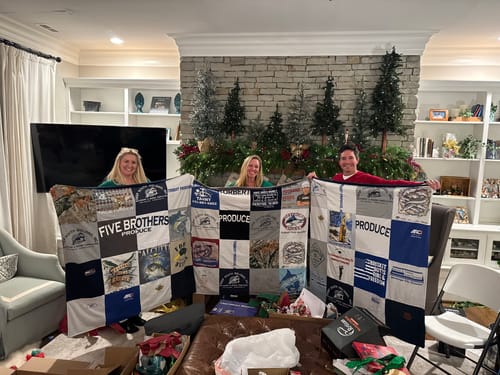 Reviewer and two others holding up three large T-Shirt Quilts in a festive living room.