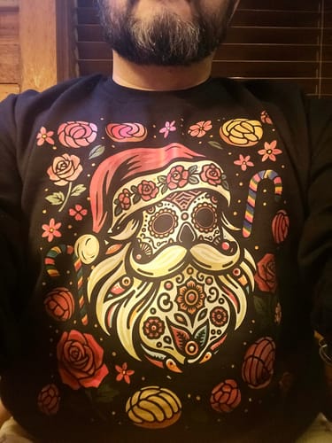 Customer wearing the black Santa Calavera Navidad Sweatshirt with its colorful sugar skull Santa design.