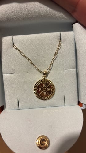 Customer's gold Engravable Compass Necklace in its presentation pouch, engraved with the initials K, S, M, and E.