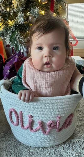 Customer's white Personalized Knitted Basket with 'Olivia' in pink yarn, shown with a baby sitting inside.
