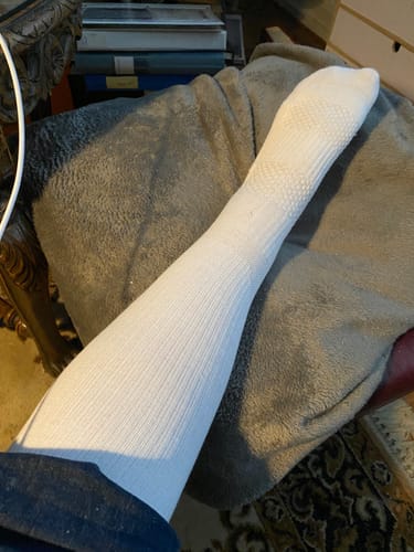 Kund visar en vit, ribbad Diasocks stödstrumpa på sitt ben.