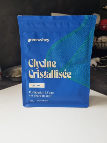 Un client montre le sachet bleu de Glycine Cristallisée posé sur une surface blanche.