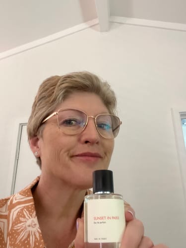 Reviewer smiling while holding a bottle of Sunset in Paris perfume.