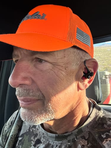 Reviewer in a camo shirt and orange hat showing the fit of the GS Extreme 2.0 earbuds.