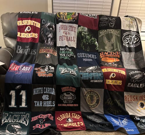 Customer's large Premium T Shirt Quilt, a patchwork of sports and graphic tees, displayed on a couch.