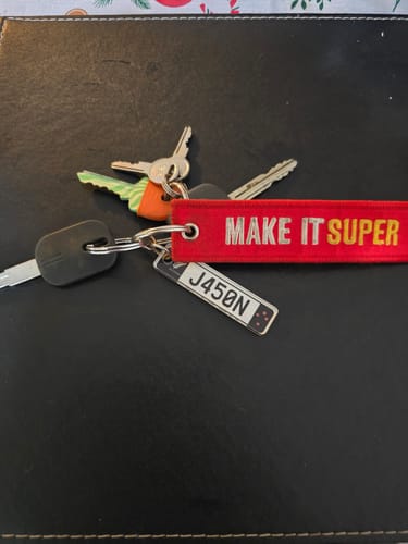Customer's car keys featuring a personalized license plate keychain and a red fabric tag on a black surface.