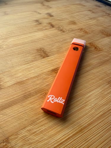 Customer's orange ROLLZ THCA Vape stick lying on a wooden surface.