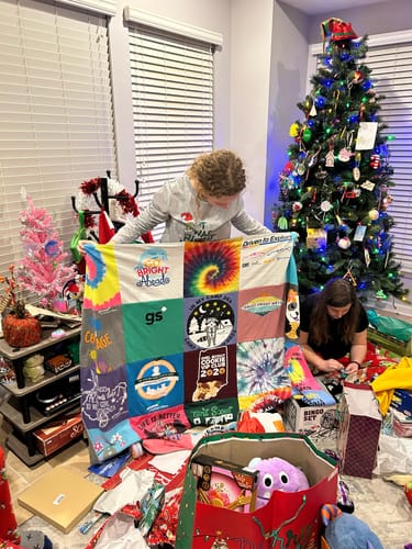 Customer holding up a colorful Premium T Shirt Quilt in a living room decorated for Christmas.