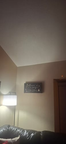 Customer's darkened 'Believe In The Magic of Christmas' sign hanging on a beige wall in their living room.