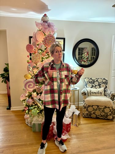 Reviewer pointing to the relaxed-fit plaid shacket they are wearing in front of a decorated Christmas tree.