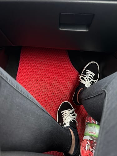 Recenzent pokazuje dopasowany, czerwony dywanik samochodowy na miejscu pasażera.