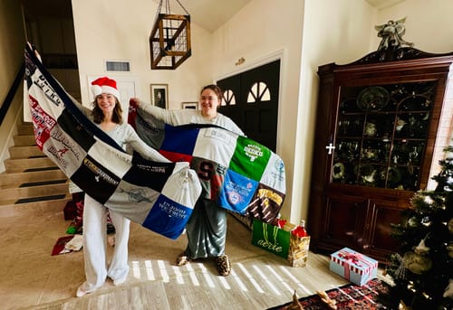 Two customers happily holding up their large Premium T Shirt Quilt in their home at Christmas.