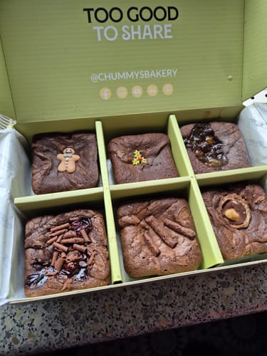 Customer's open postal brownie box showing six different brownies with festive Christmas decorations inside.
