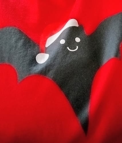 Close-up of customer's red Batty For Christmas T-Shirt, showing a smiling bat graphic wearing a Santa hat.