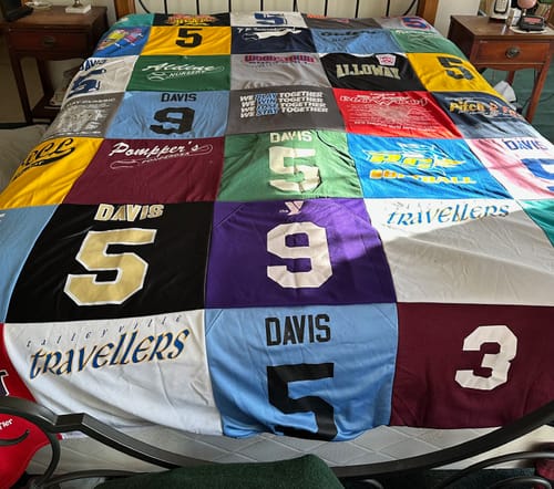 Customer's colorful Premium T-Shirt Quilt made from sports jerseys with numbers and names, spread across a bed.