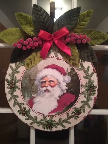 Customer's Round DecoExchange Sign Extender decorated with a Santa image, a red bow, and green leaves, used as a door hanger.