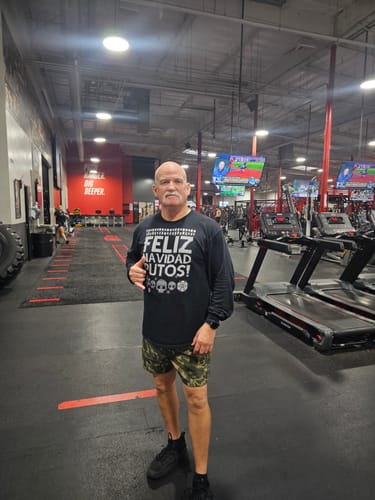 Reviewer standing in a gym wearing the black Feliz Navidad Putos OG Navidad Sweatshirt.