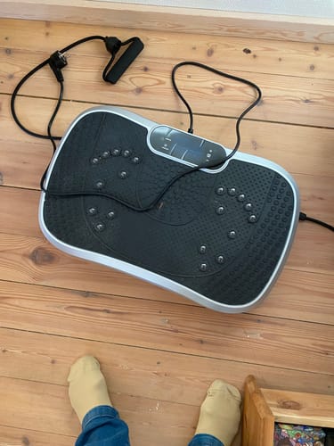 Kundes sorte vibrationstræner med elastikbånd på et trægulv.