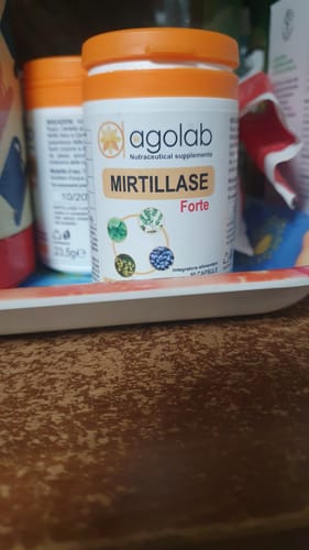 Cliente mostra il flacone bianco di Mirtillase Forte con tappo arancione su un tavolo.