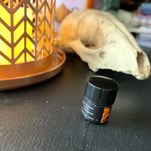 Reviewer's small bottle of Pumpkin Spice Pandemic perfume oil next to a glowing lantern and an animal skull.