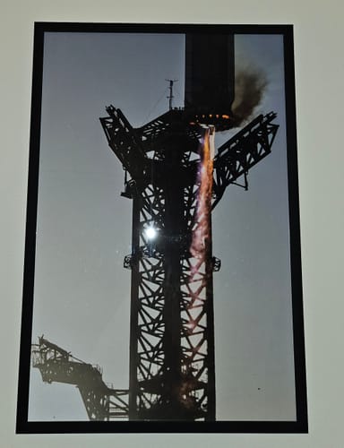 Customer's framed 'Welcomed Back with Open Arms' print on a white wall, showing a dramatic rocket booster catch.