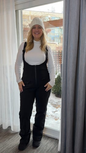 Reviewer standing indoors wearing the Women's Black Slim Fit Fully-Sealed Ski Bibs over a white shirt.