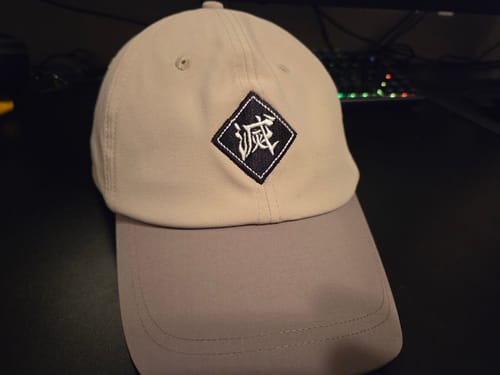 Customer's embroidered Big Cross Training Hat in light tan with a grey brim, seen up close on a desk.