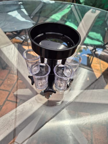 Customer's black Wet Pussy Pourer with some liquid in the top funnel, shown with six shot glasses on a table.