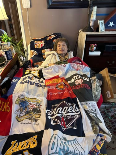 Customer shows a person smiling while wrapped in a large Premium T Shirt Quilt made from various t-shirts.