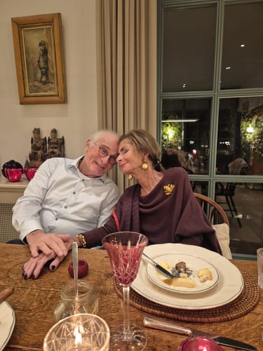 Reviewer wearing the Amethyst Plum Asymmetric Draped top, holding hands with a person at a table.