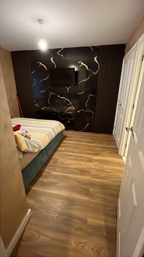 Customer's bedroom with dark Acoustic Slatted Wall Panels installed vertically on a stylish feature wall around a TV.