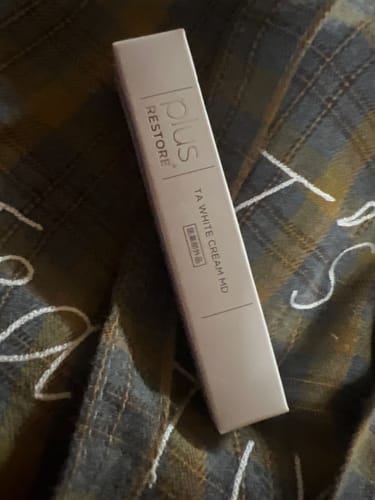 レビューアーによる、柄の布の上に置かれたTAホワイトクリームMDの外箱。