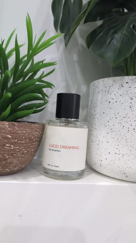 Customer's Lucid Dreaming fragrance bottle displayed on a white shelf between two potted plants.