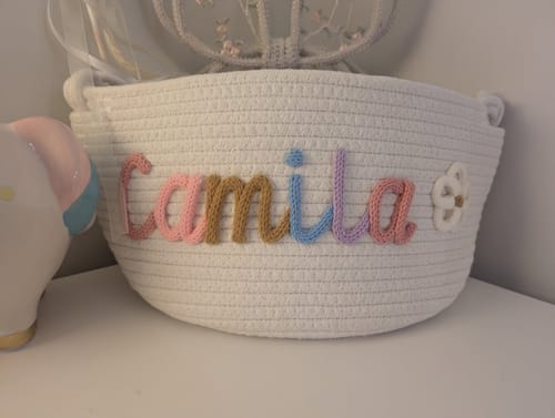 Customer's white Personalized Knitted Basket with the name 'Camila' in multicolor yarn and a flower icon.