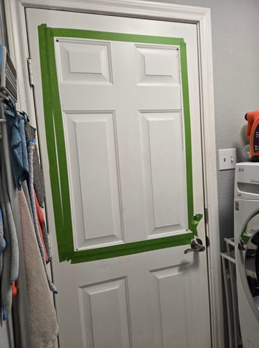 Customer's white door with green tape outlining the area for the Venting 1 Lite Glass and Frame Kit installation.
